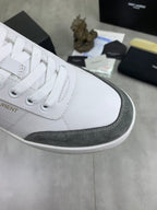 Unisex low-top sneakers close-up: white leather, gray trim, lace eyelets.
