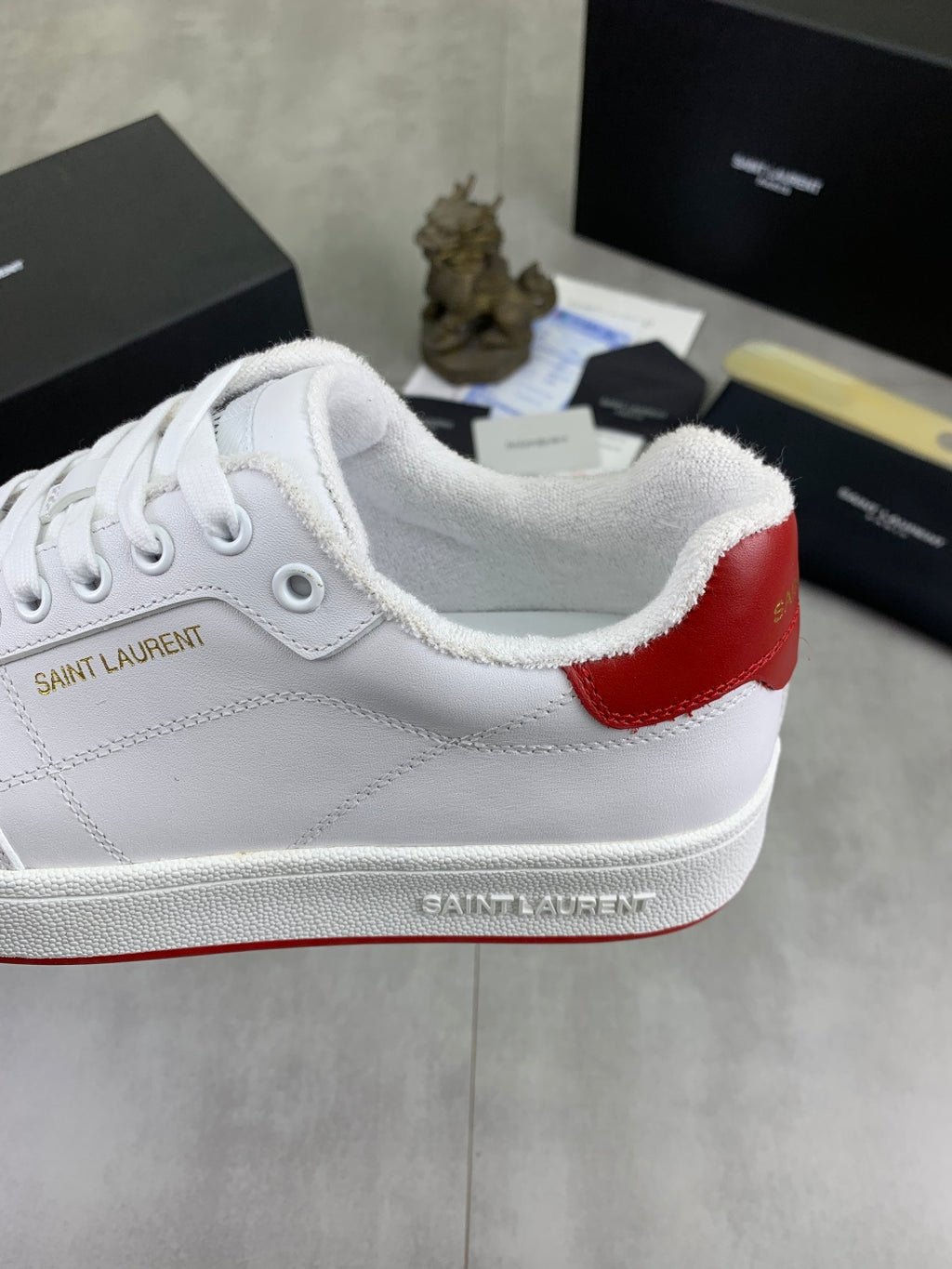 White sneaker with red heel patch, cushioned collar, and lace-up front.