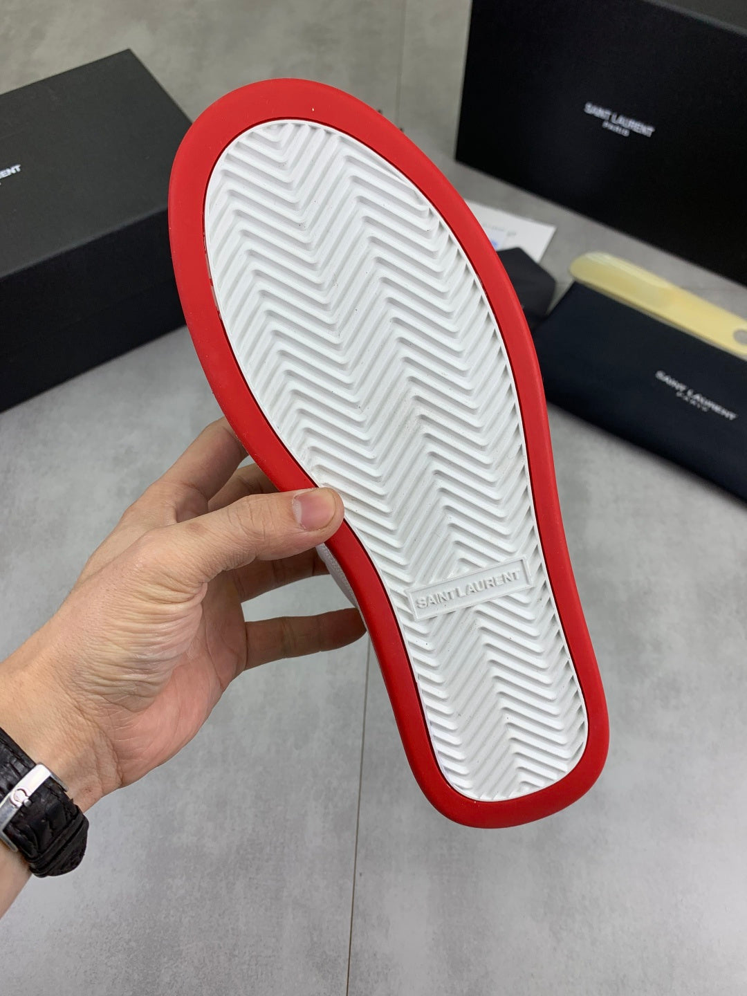 White rubber outsole with red border and chevron tread, held in hand.
