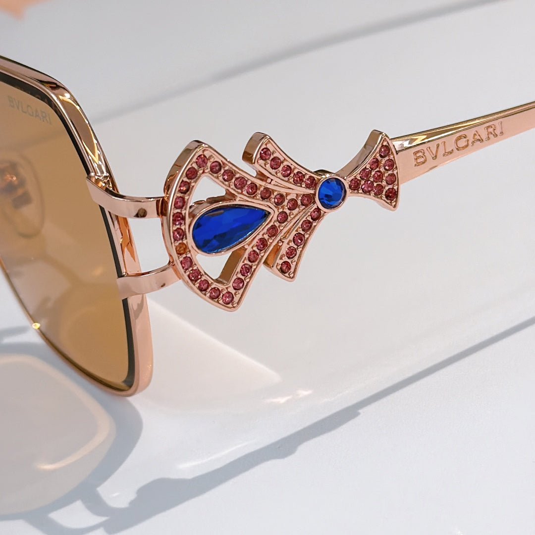 Bvlgari sunglasses close-up: gold frame with red jeweled crown and blue center gem