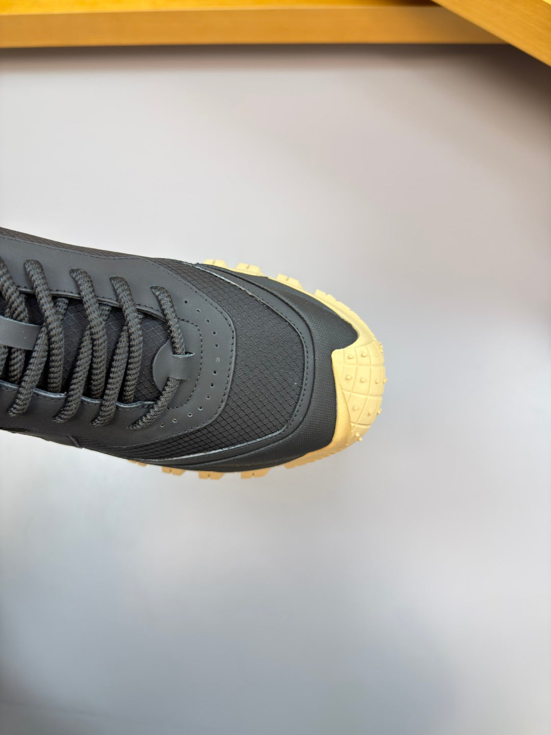 Moncler sneaker close-up of toe and side: dark navy upper with gum yellow trim