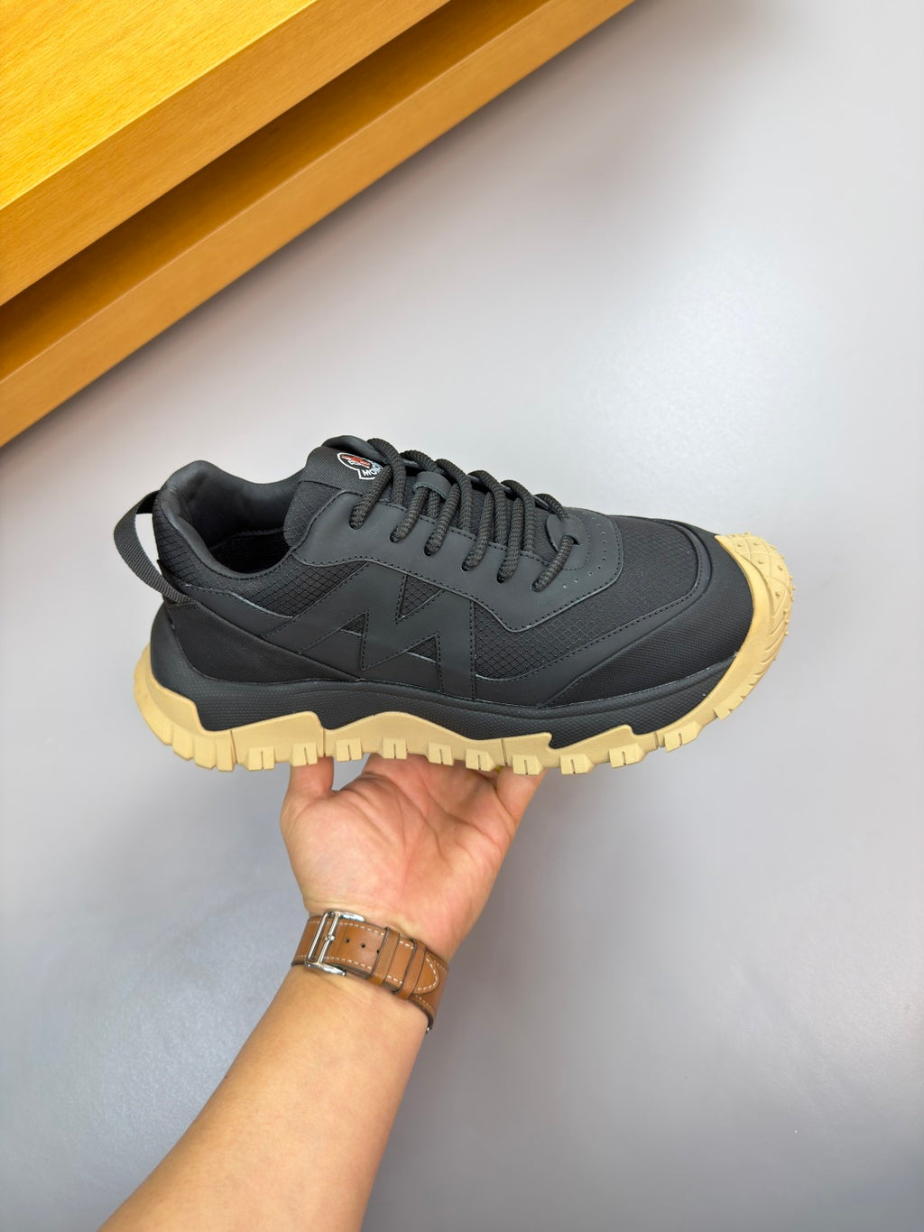 Moncler sneaker held in hand: dark navy upper, lace-up front, gum yellow sole