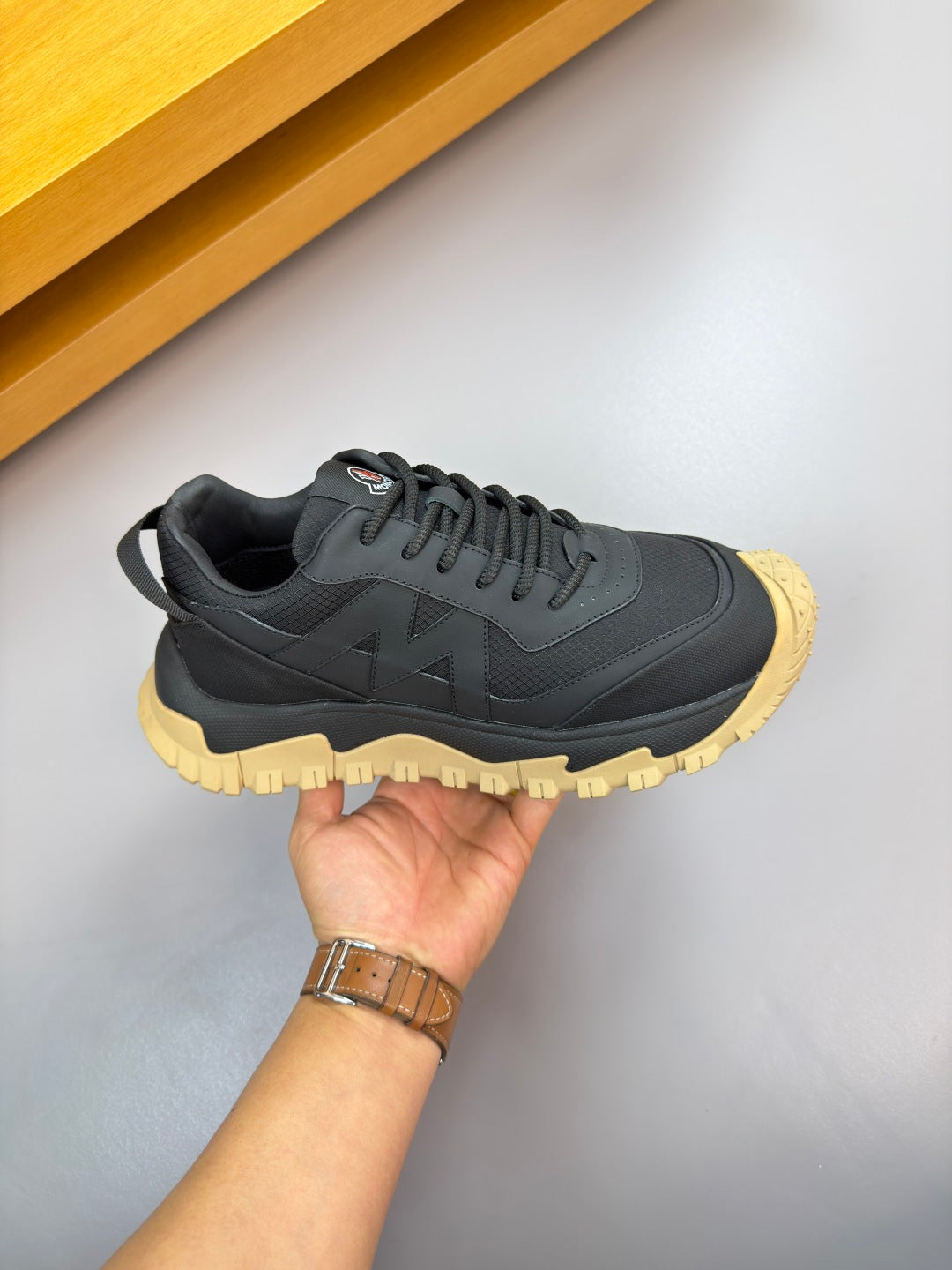 Moncler sneaker held in hand: dark navy upper, lace-up front, gum yellow sole