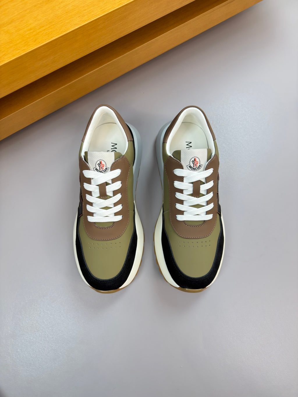 Sneakers, olive and black uppers with white laces, viewed from above.