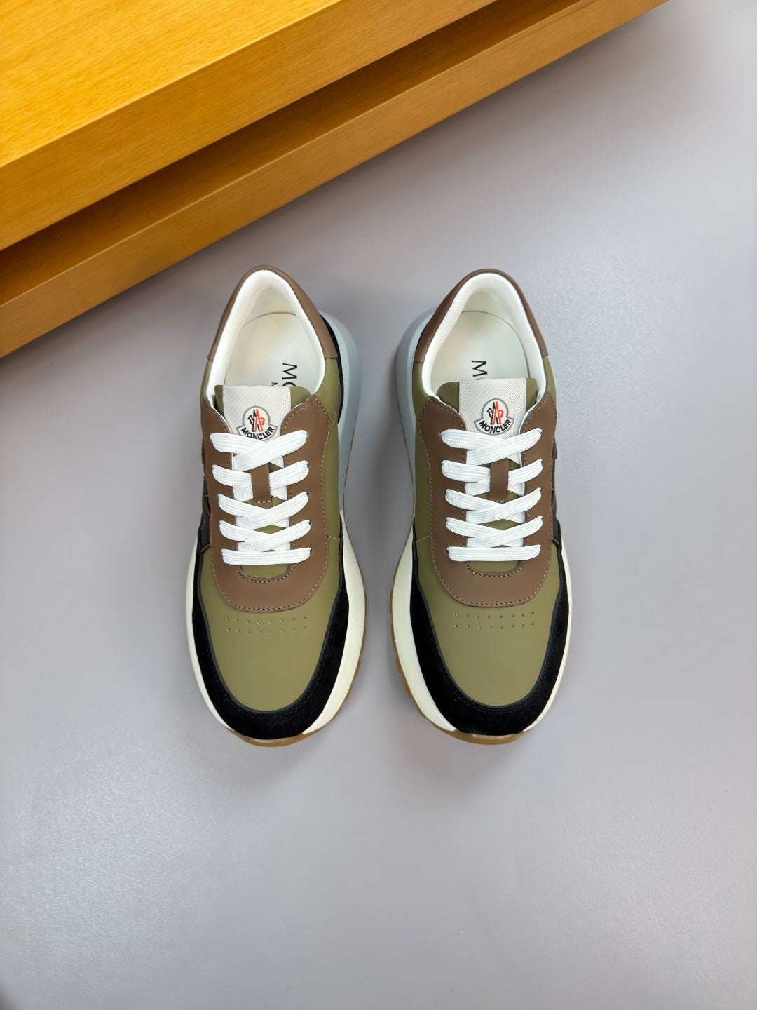 Sneakers, olive and black uppers with white laces, viewed from above.