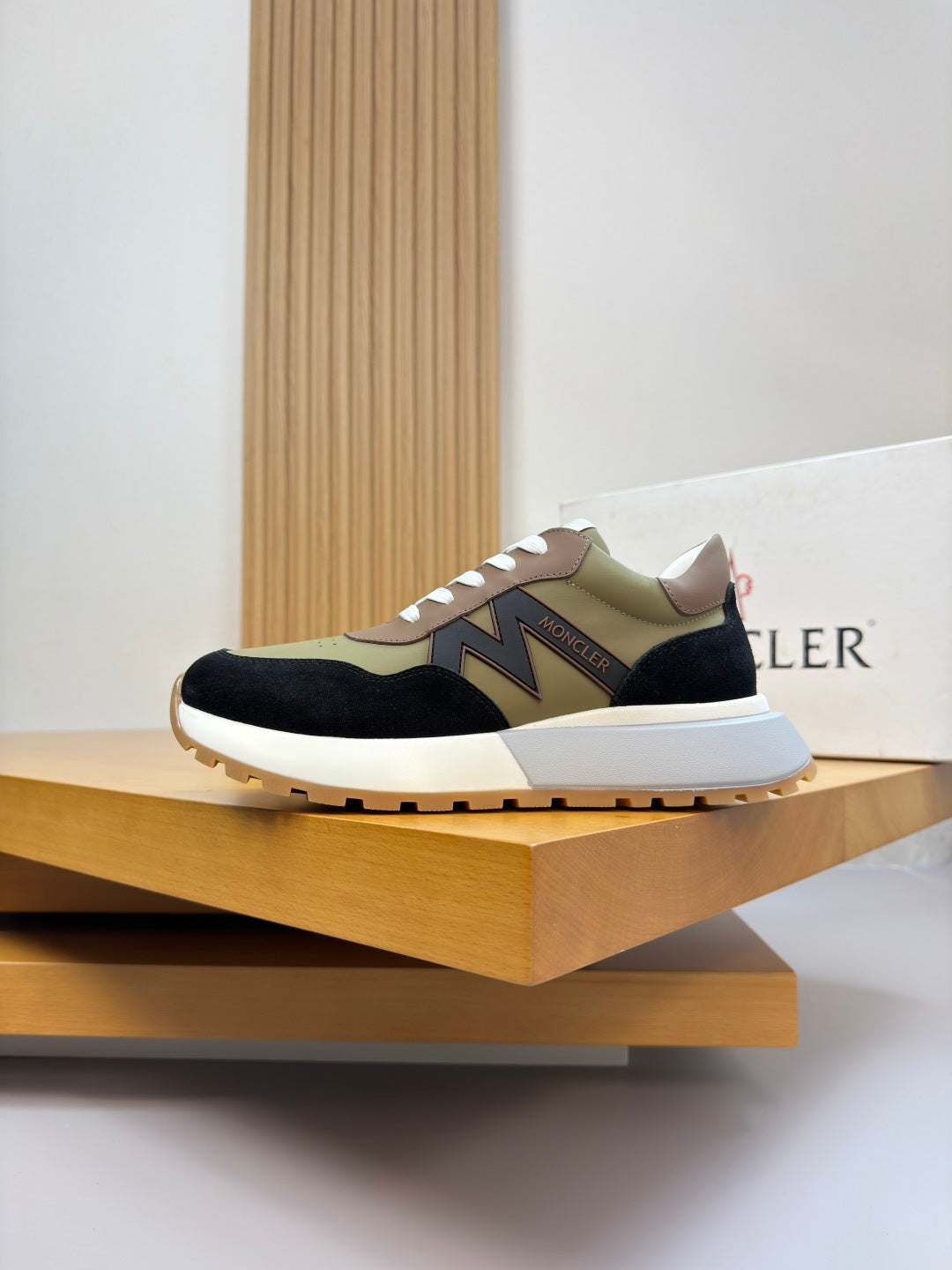 Low-top sneakers on display with olive, black, and cream panels and white laces.