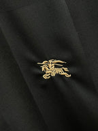 Embroidered crest logo on dark black shirt fabric in gold-tone thread