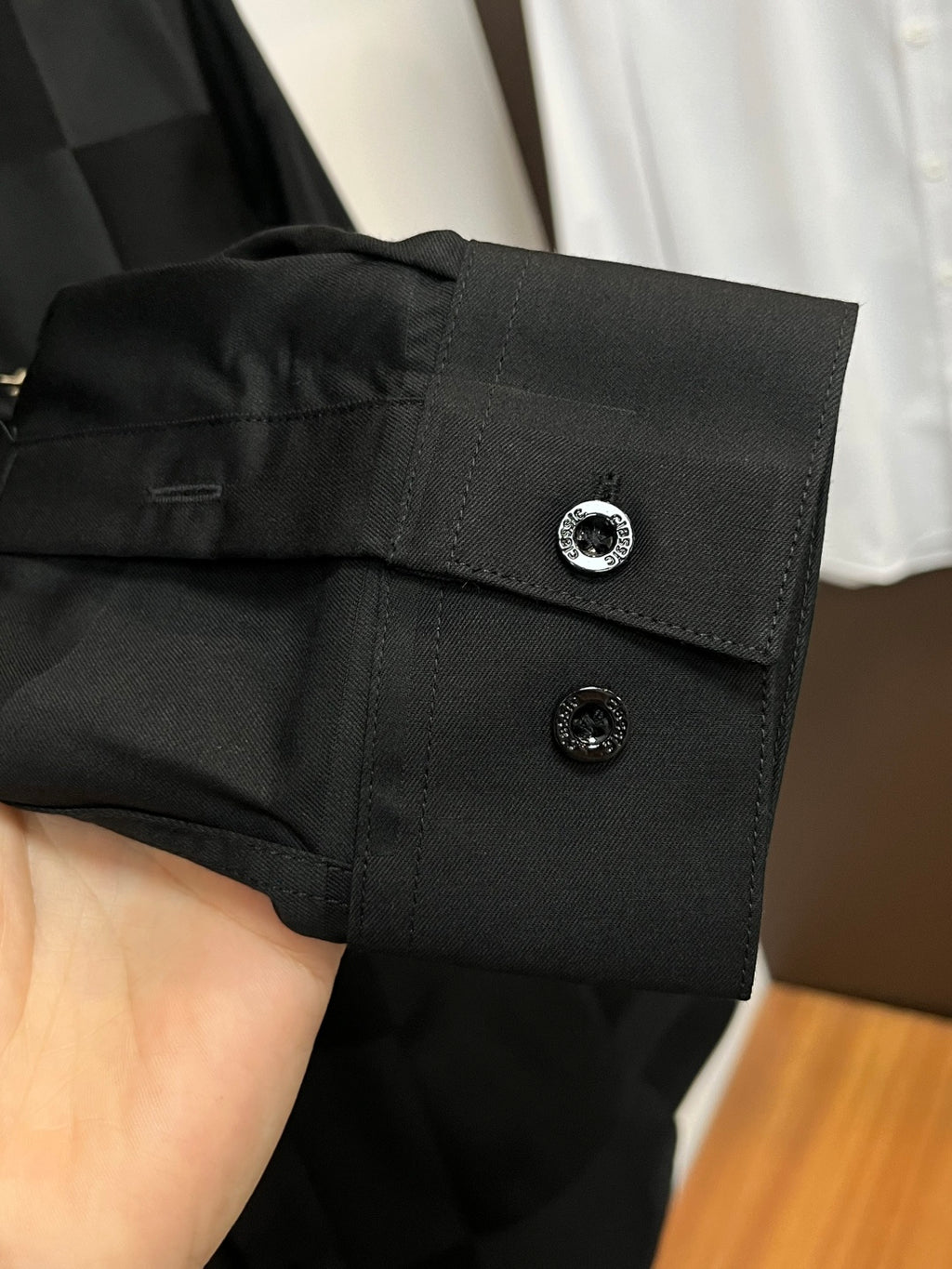 Dark black shirt cuff with two buttons and round emblem detail
