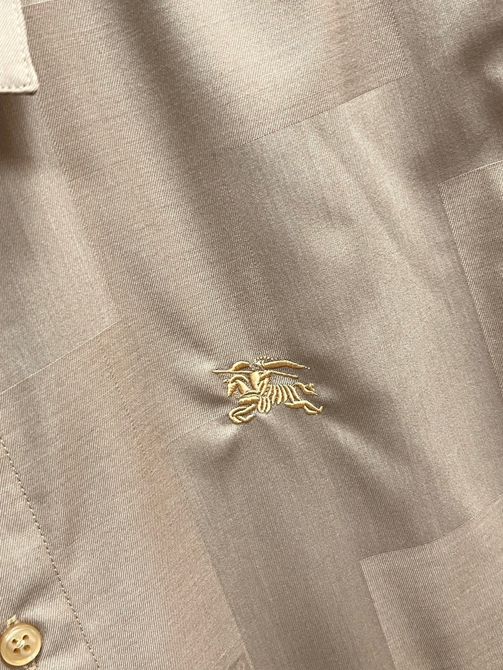 Beige shirt fabric with small gold embroidered crest at the chest