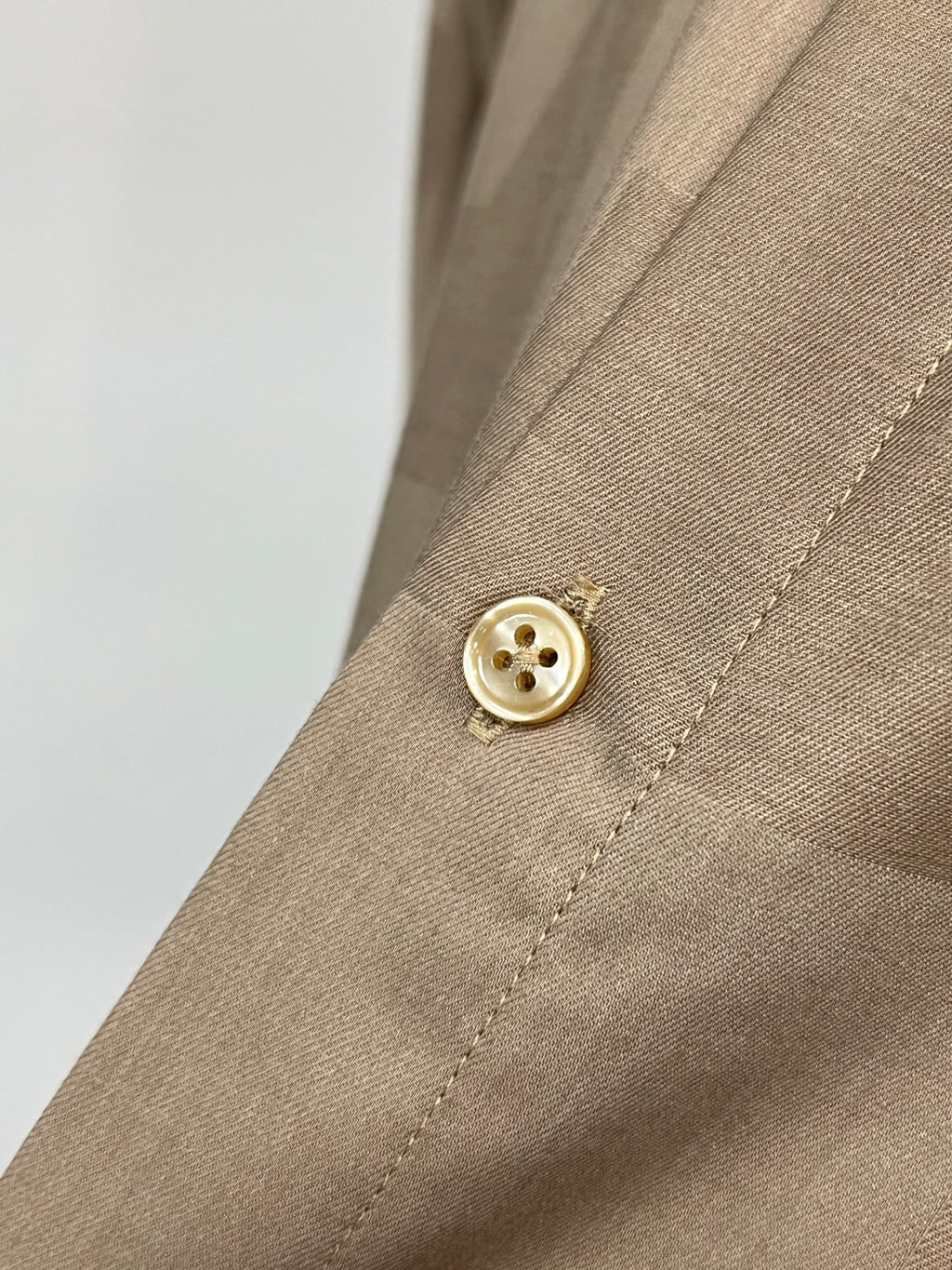 Beige shirt cuff with round button and visible stitched seam