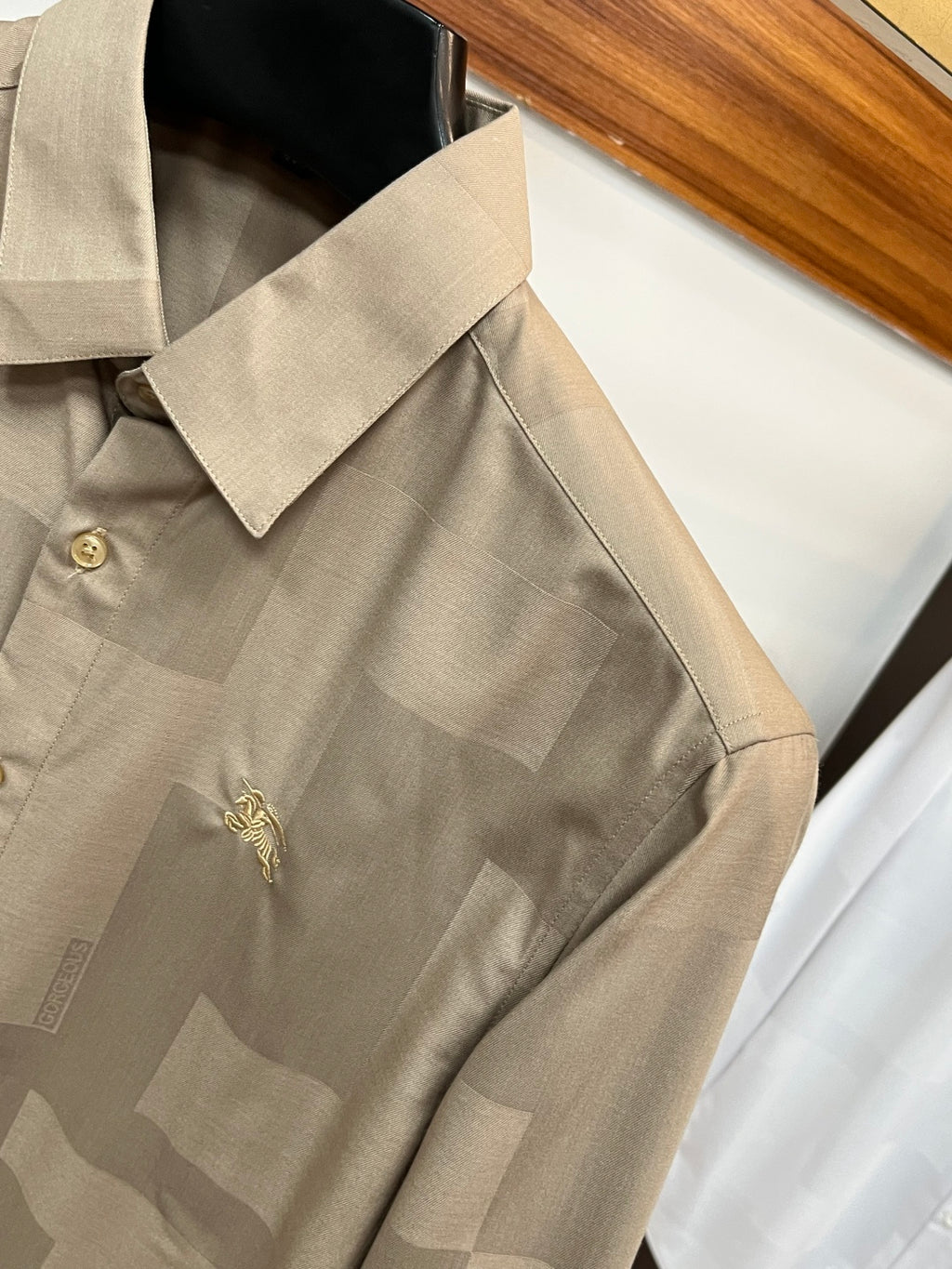 Beige long-sleeve button-up shirt with embroidered emblem on the chest