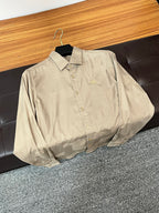 Beige long-sleeve button-up shirt with front buttons and small chest emblem