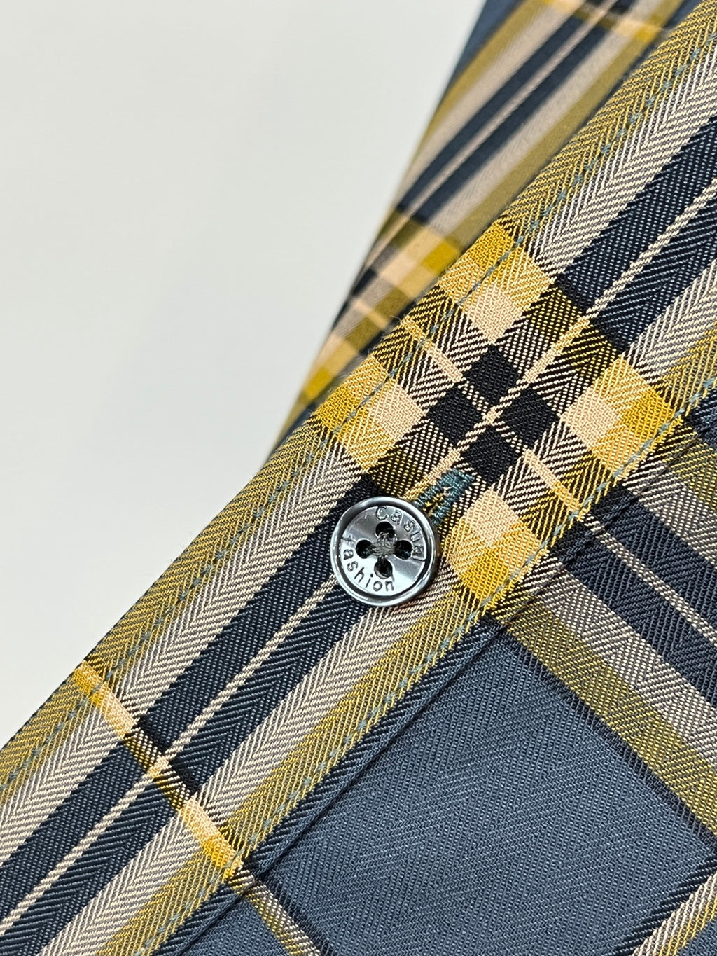Round button on plaid dress shirt placket in dark blue, white, and yellow