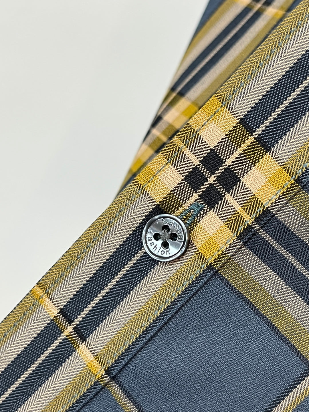 Round button on plaid dress shirt placket in dark blue, white, and yellow