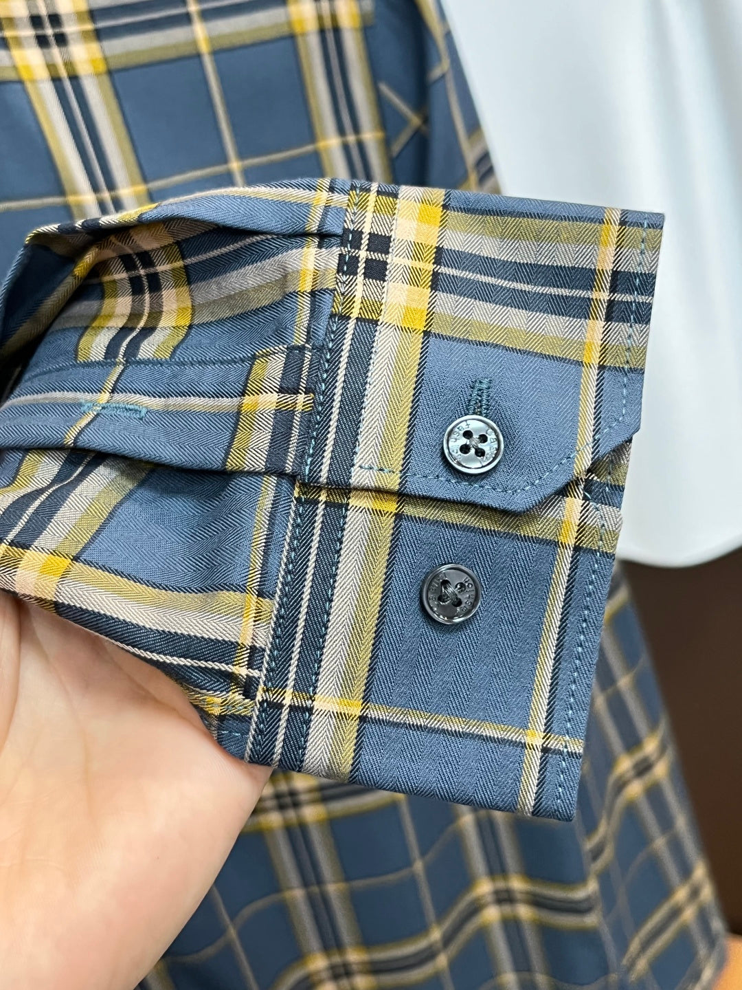 Buttoned cuffs and sleeve placket of blue plaid dress shirt with yellow accents