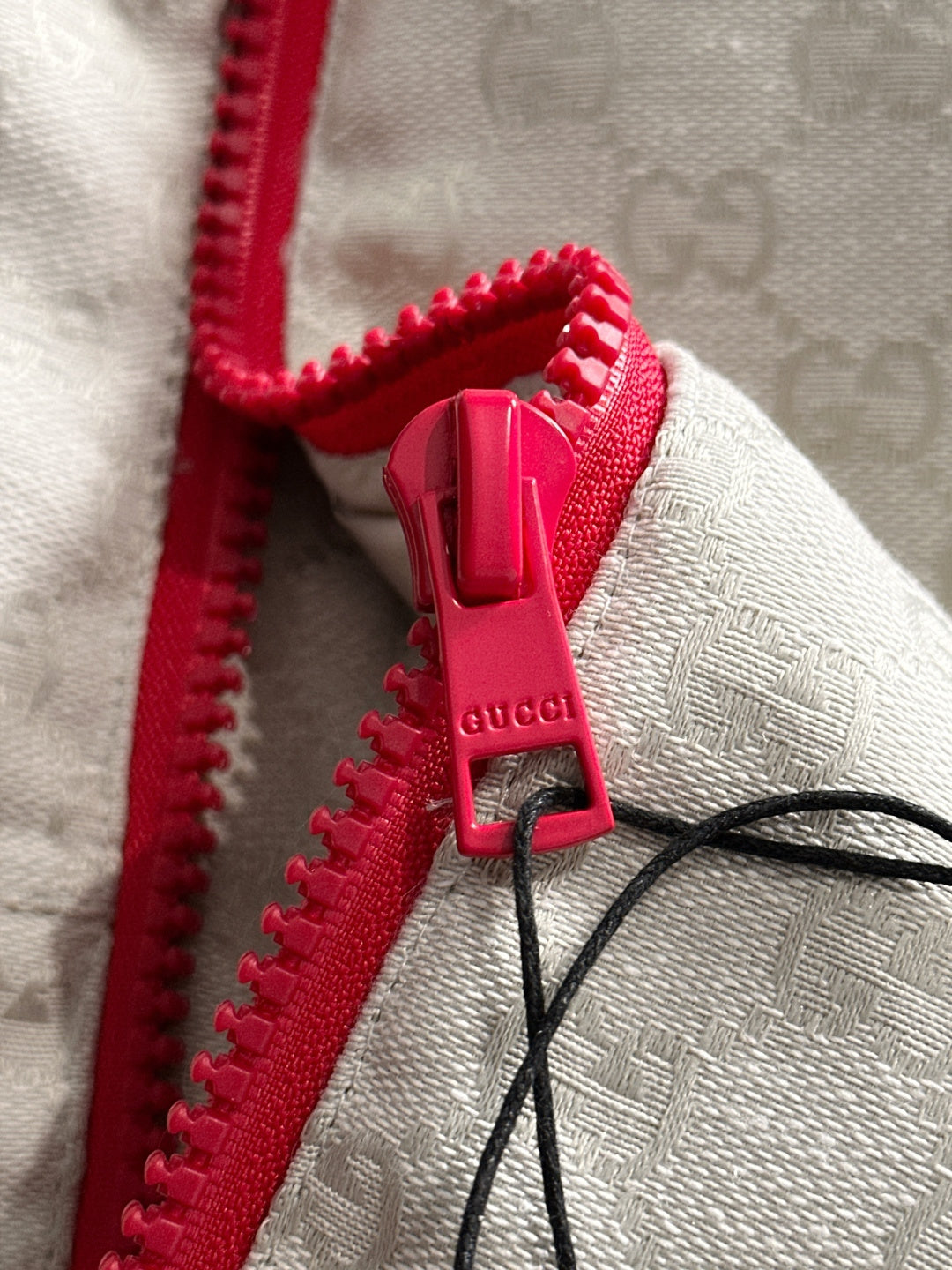 Gucci jacket zipper close-up, red zipper pull on light-gray monogram