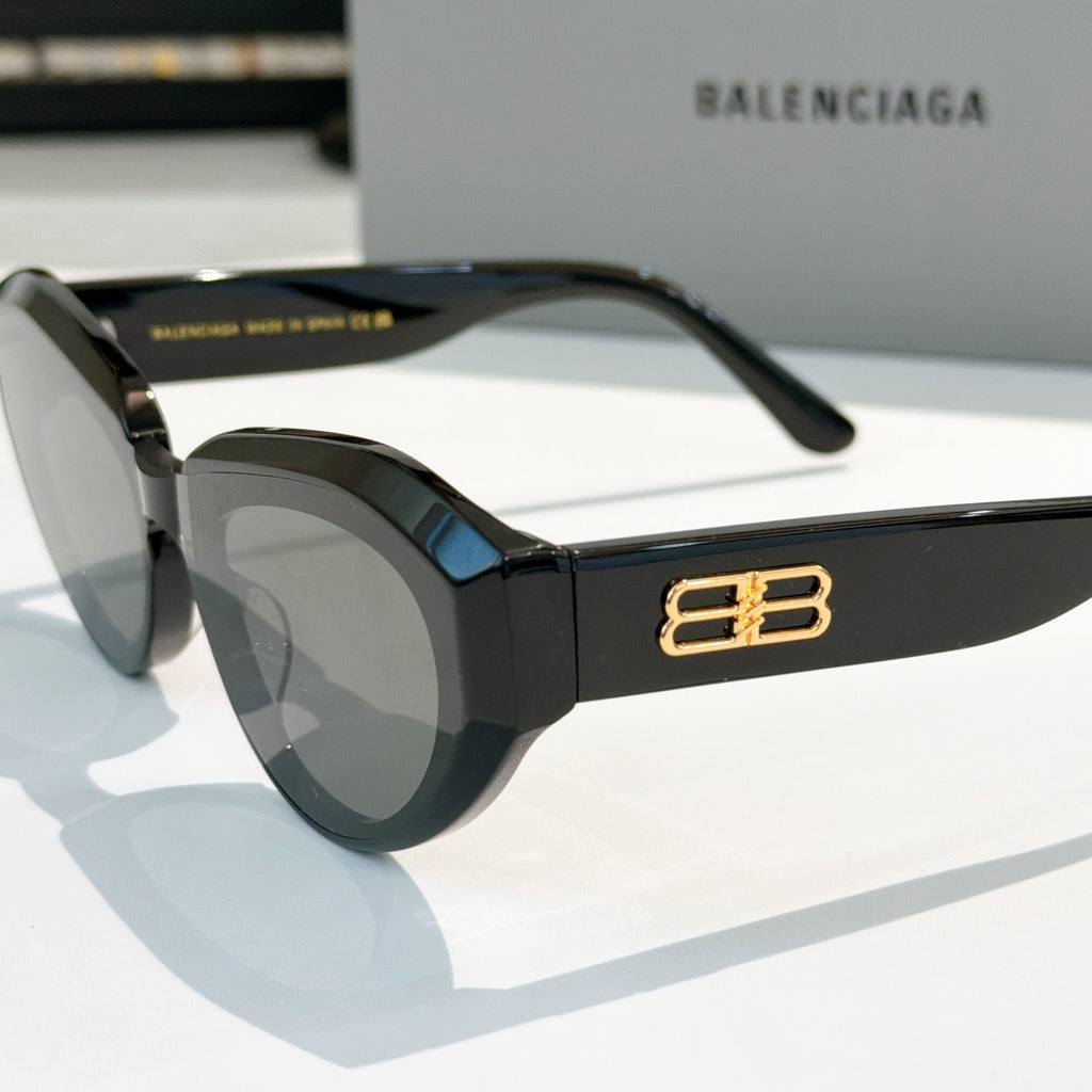 Balenciaga sunglasses, black frames close-up with gold B logo on temple