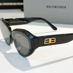 Balenciaga sunglasses, black frames close-up with gold B logo on temple