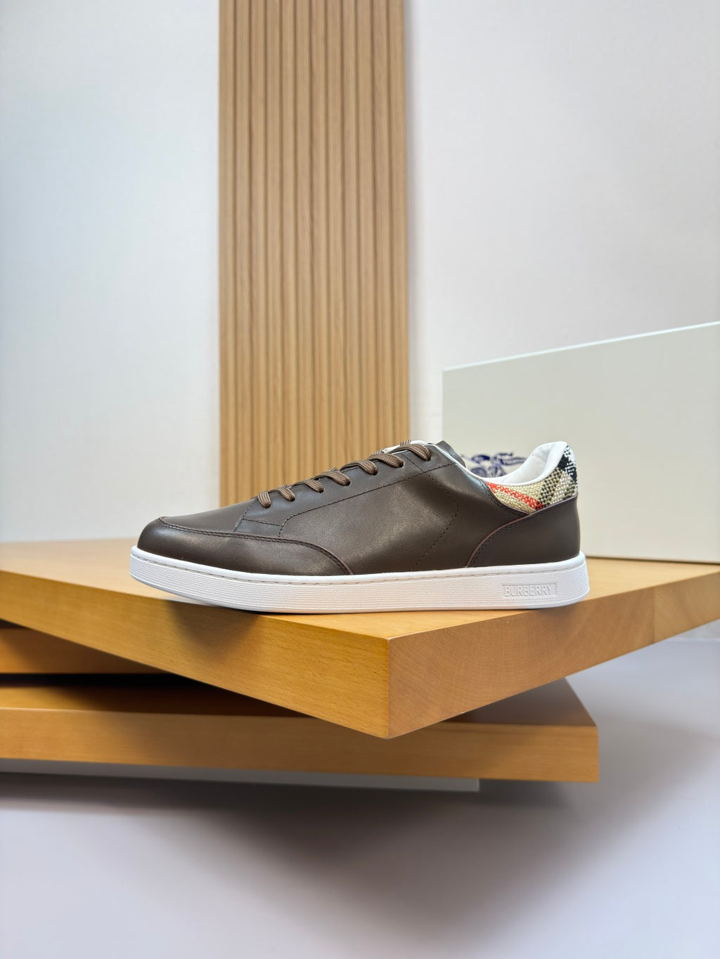 Brown low-top sneakers on display shelf with white sole and lace-up front