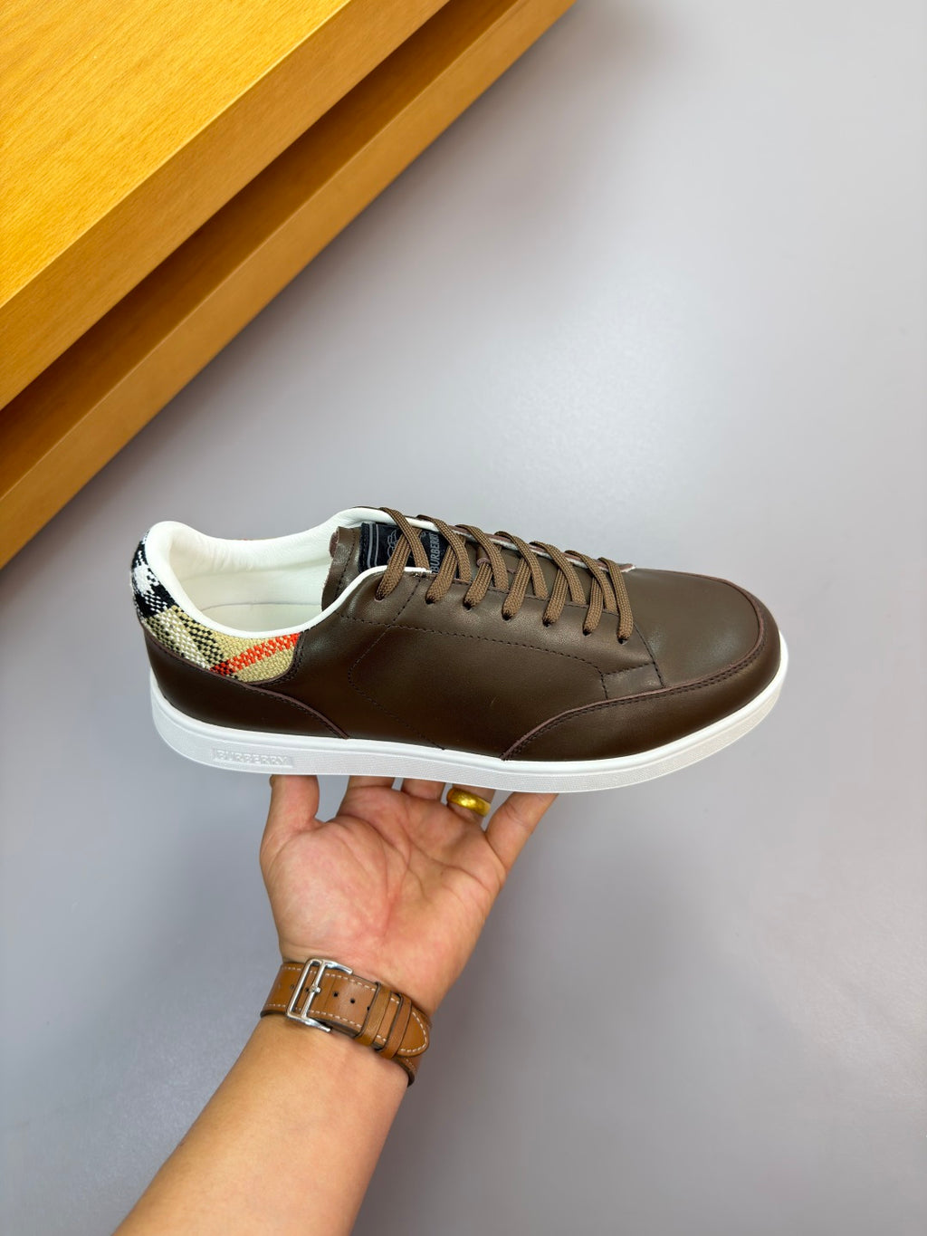 Dark brown lace-up sneakers held in hand, with white sole and patterned collar lining