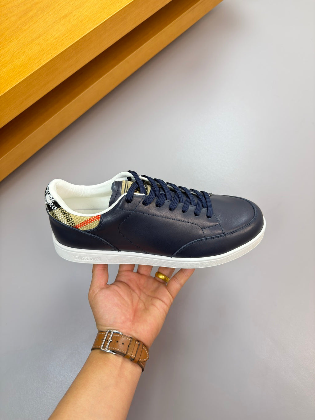 Burberry navy sneaker held in hand, lace-up front with white rubber sole