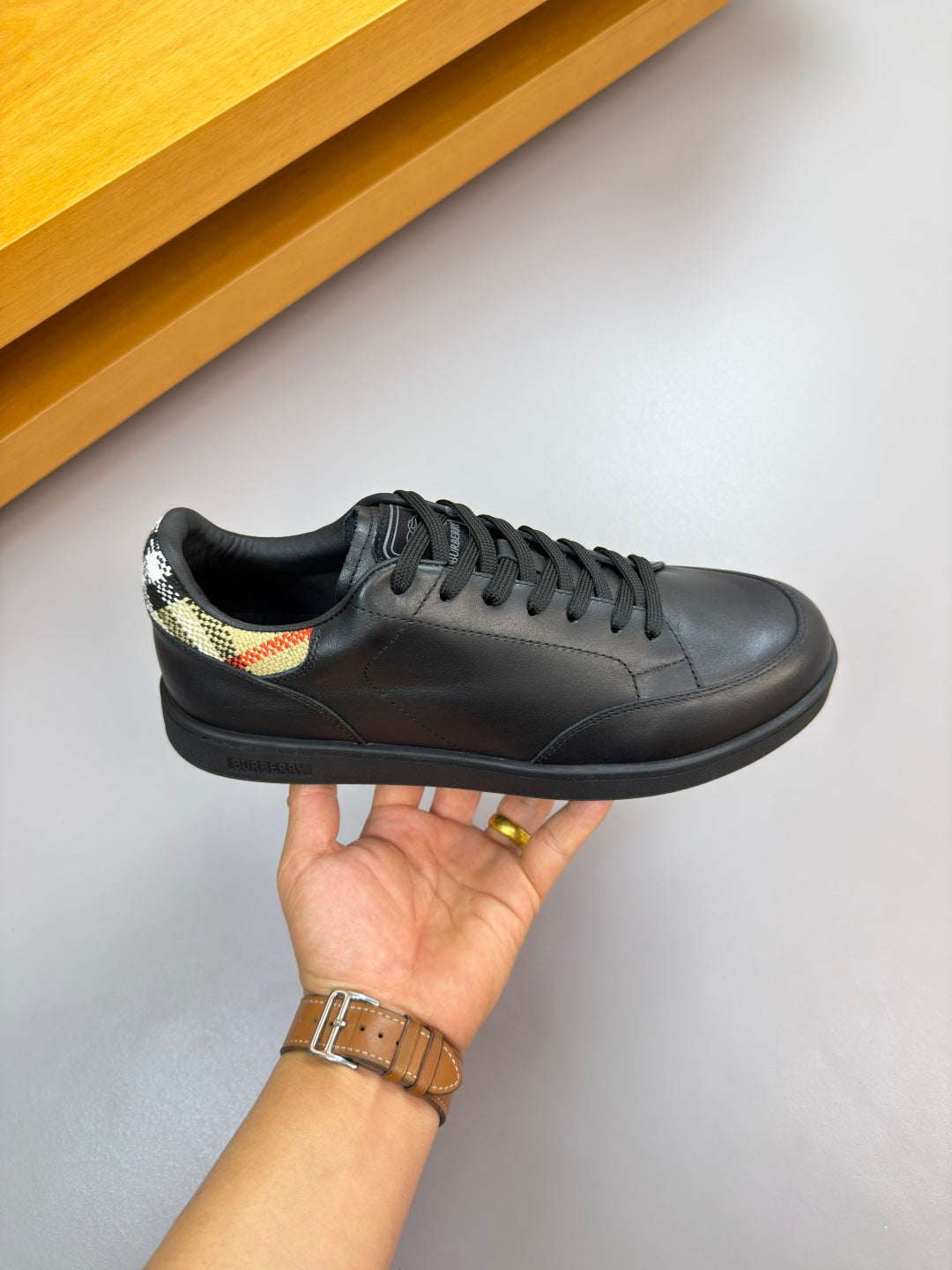 Burberry black leather sneaker held by hand, lace-up with multicolor collar detail