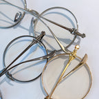 Set of round metal eyeglasses in chrome and gold tones with bow-shaped temple details.