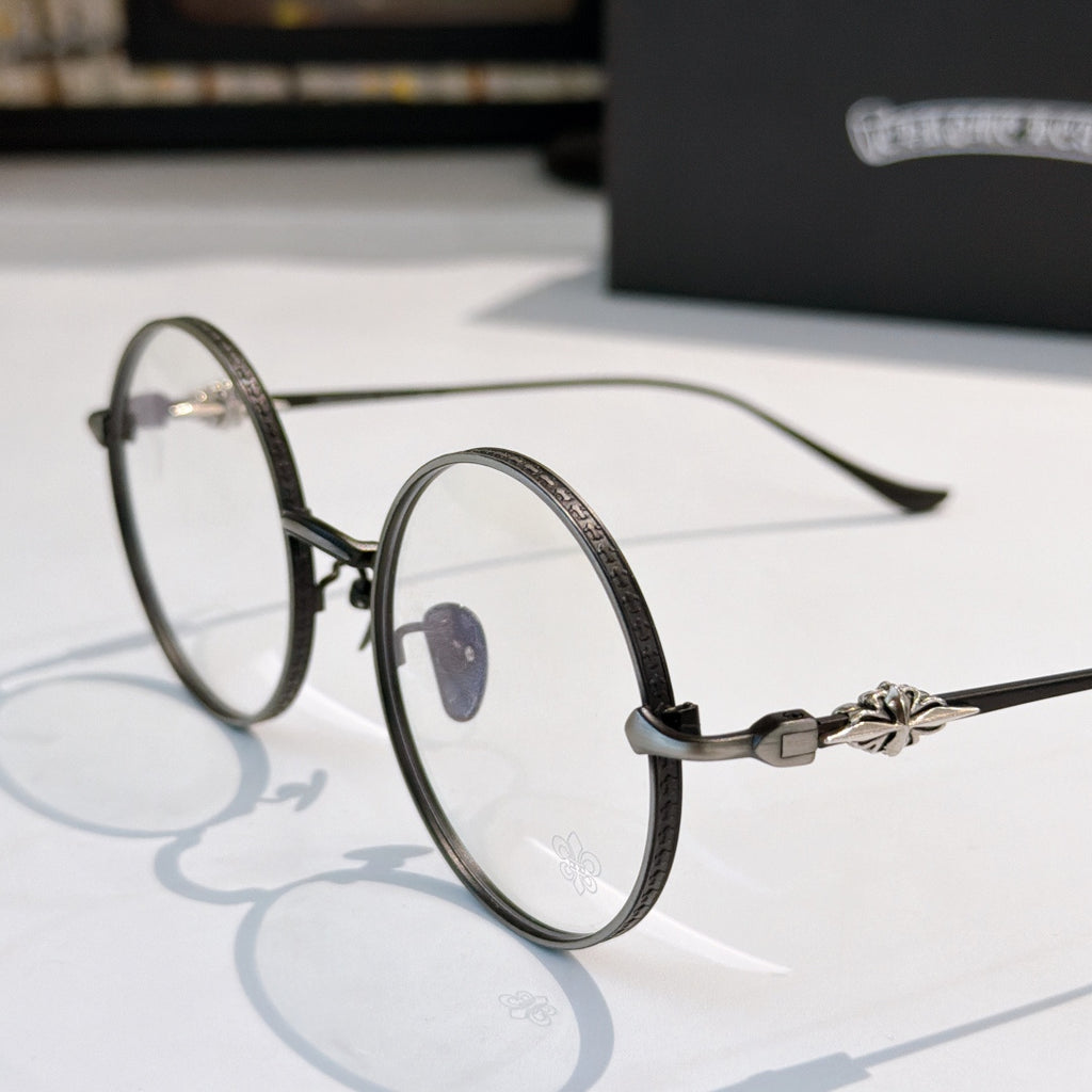 Round eyeglasses with dark metal rim, blue nose pad detail, flower decor on temple.