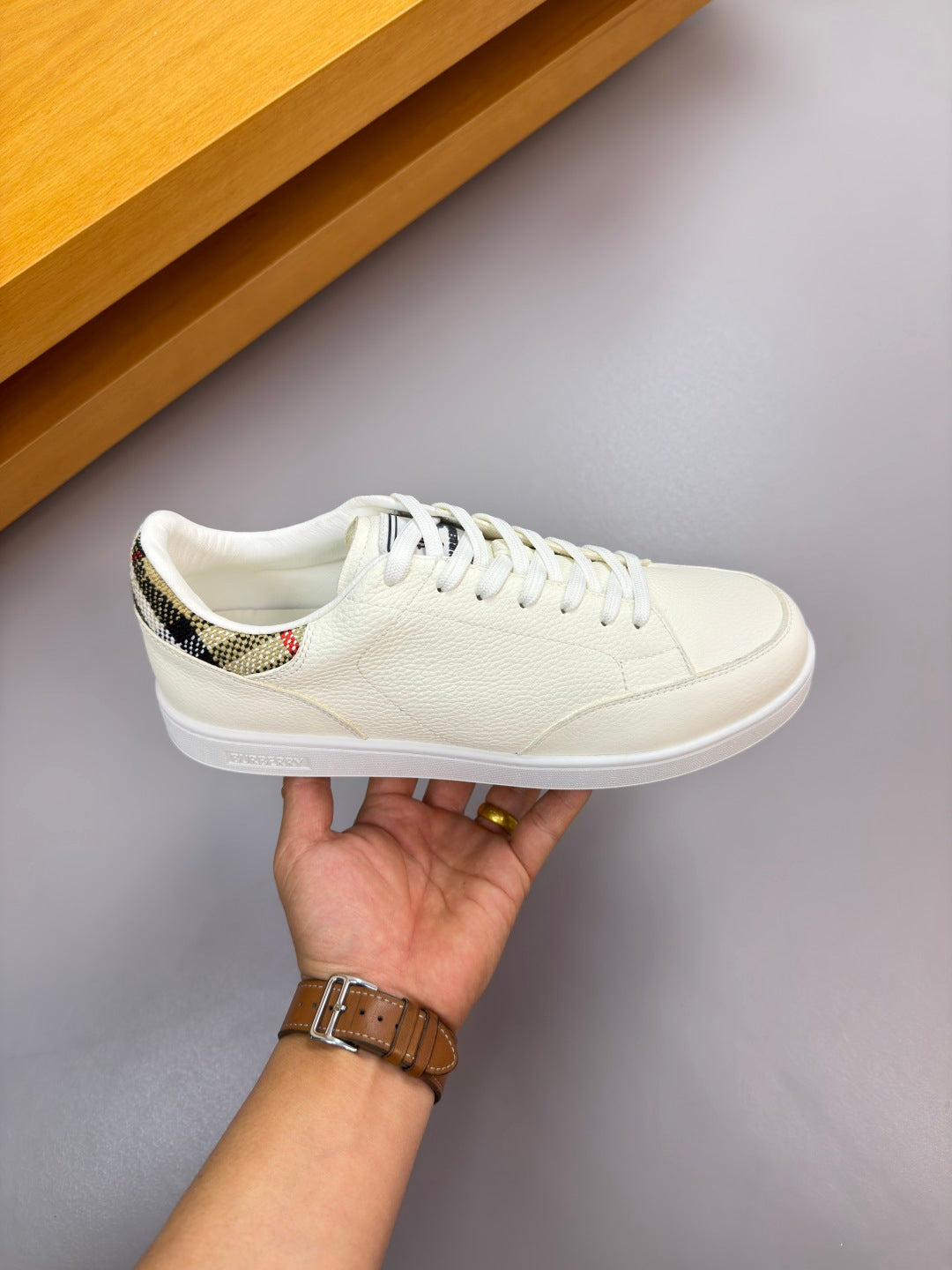 Burberry white sneaker held by hand, lace-up front view