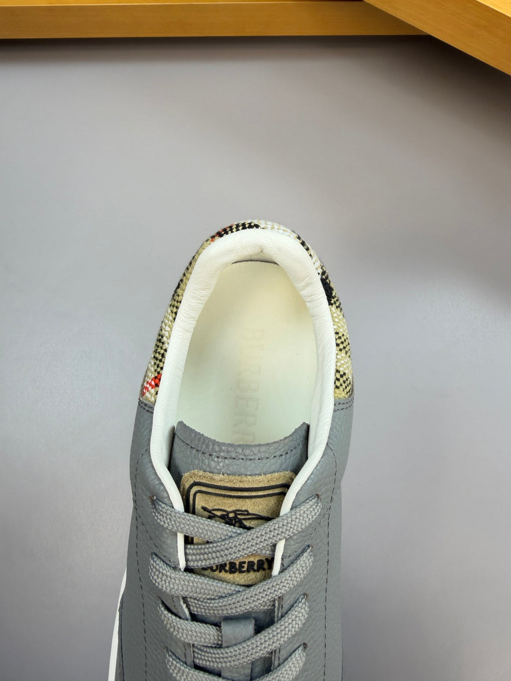 Light gray sneaker with plaid lining at collar and yellow and black logo patch