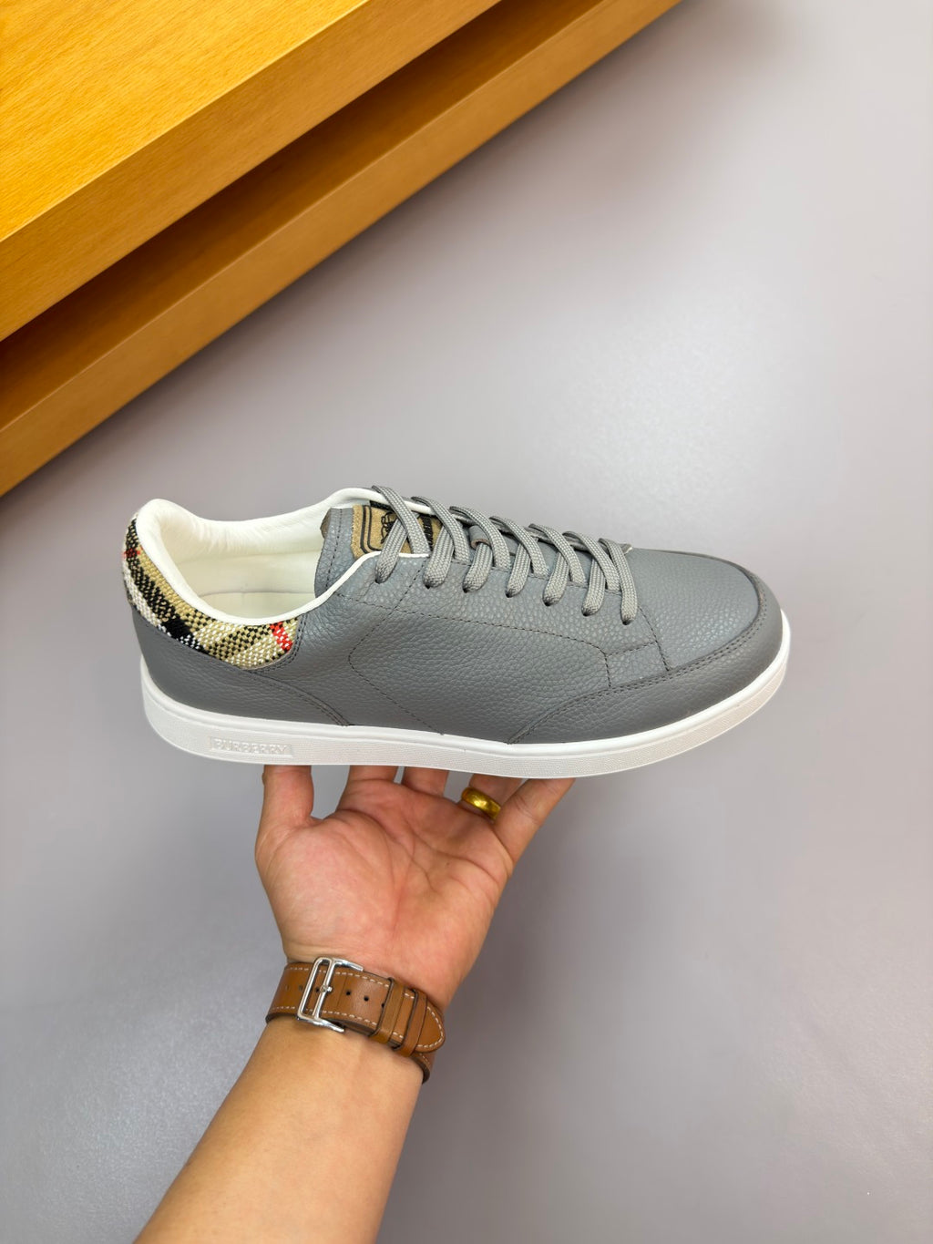 Gray leather low-top sneaker held up, check-pattern collar lining and laces