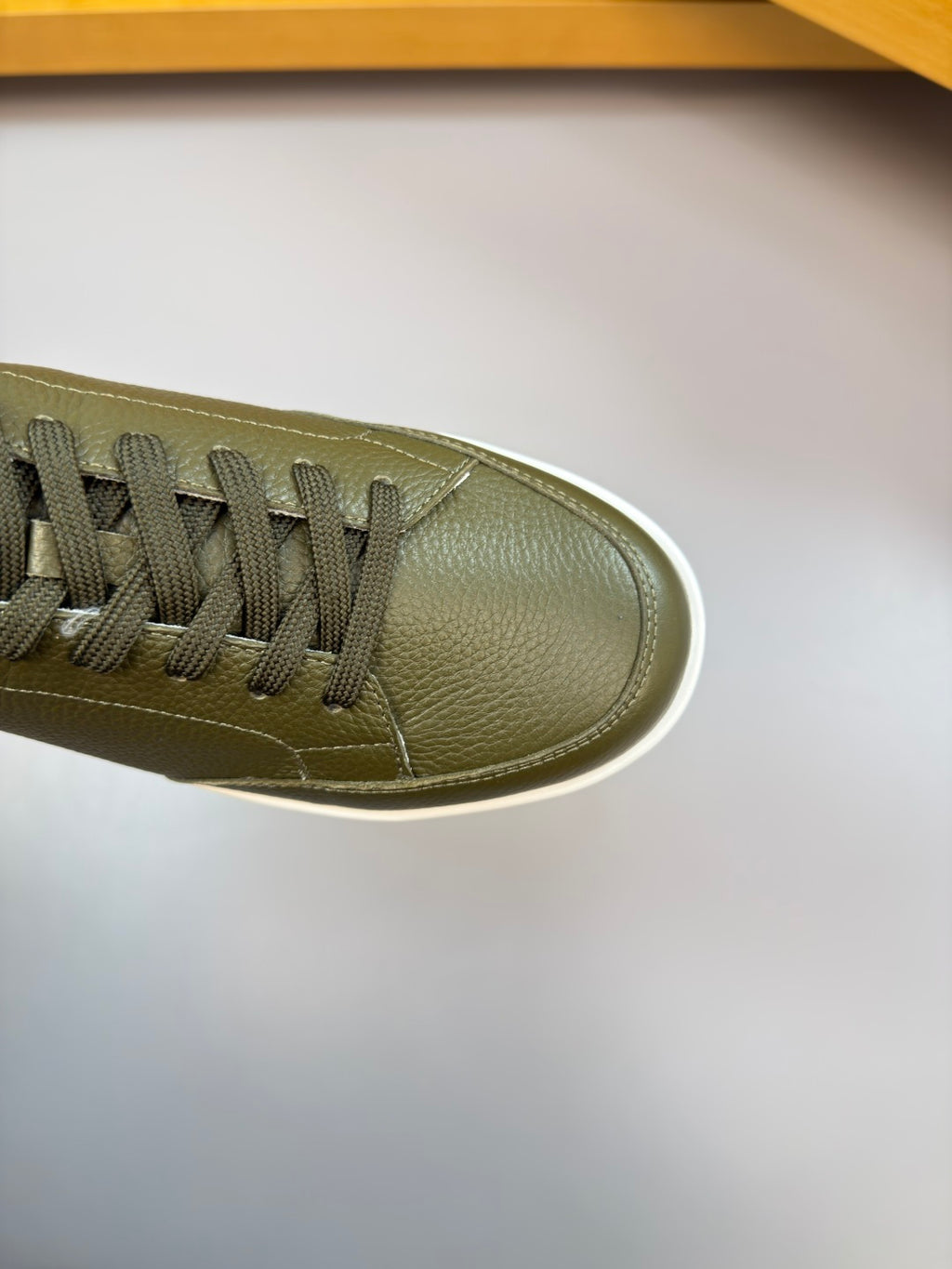 Olive green sneaker toe and side profile with black lace eyelets and white rubber edge