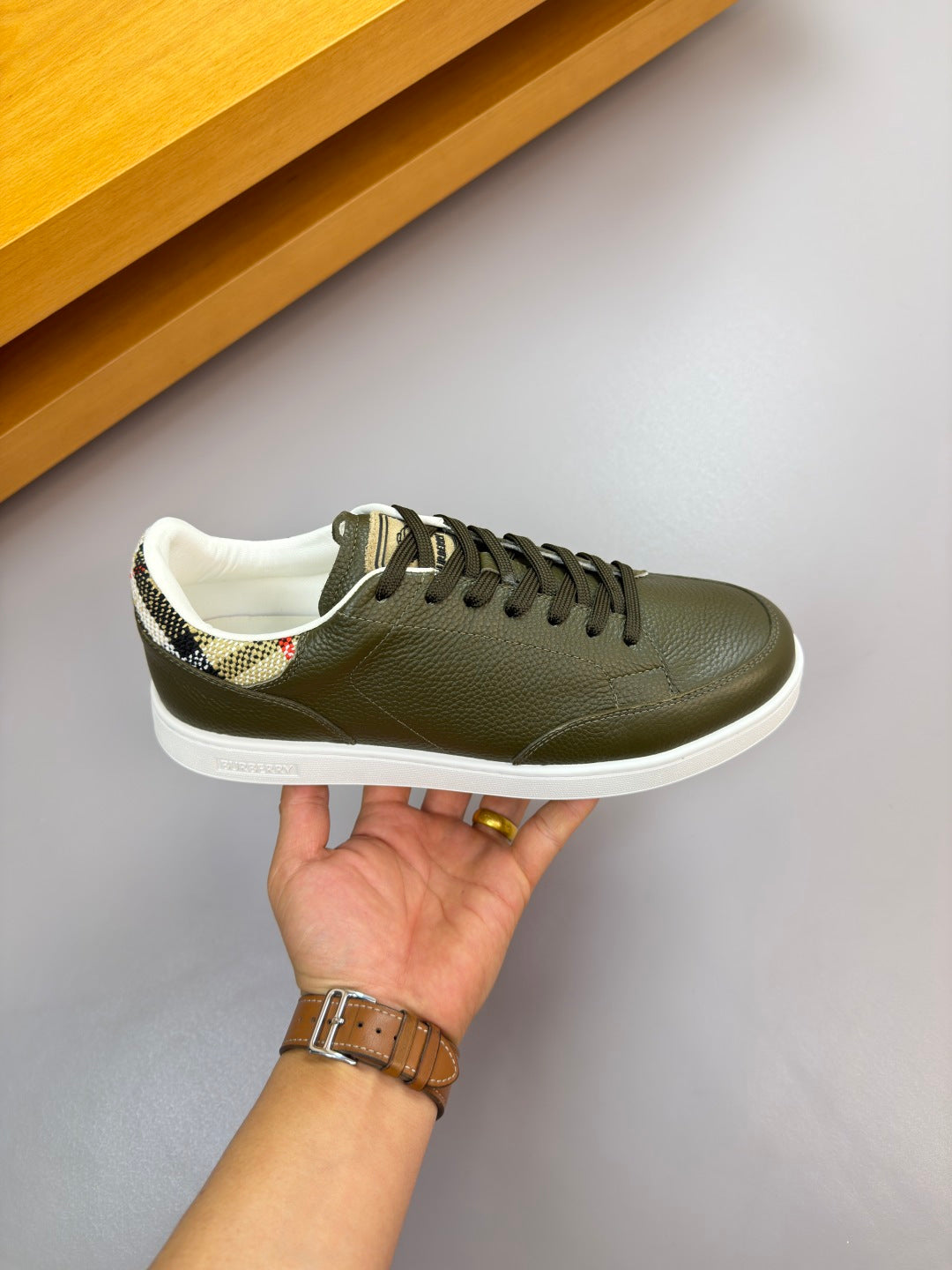 Olive green lace-up sneaker with white sole and patterned collar lining, held in hand