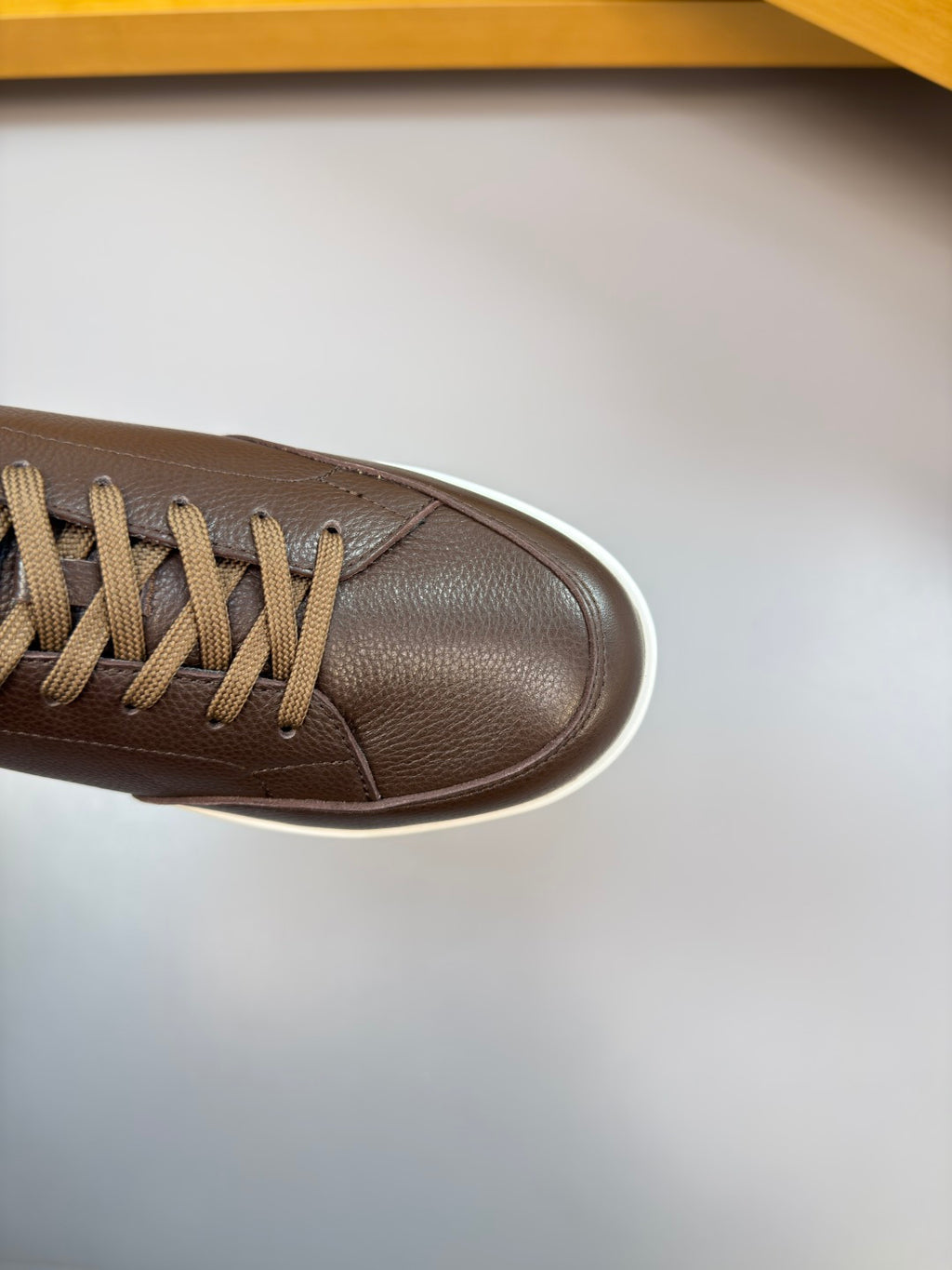 Brown sneaker toe with lace-up front and smooth leather texture, white sole edge