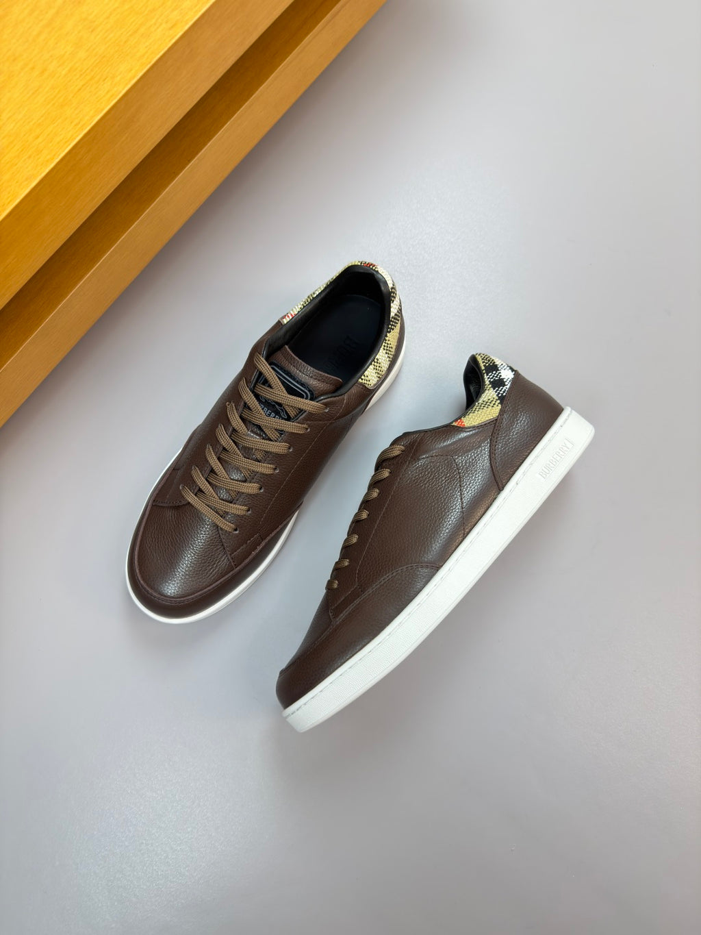 Brown leather low-top sneakers with white sole and plaid collar accent, side view