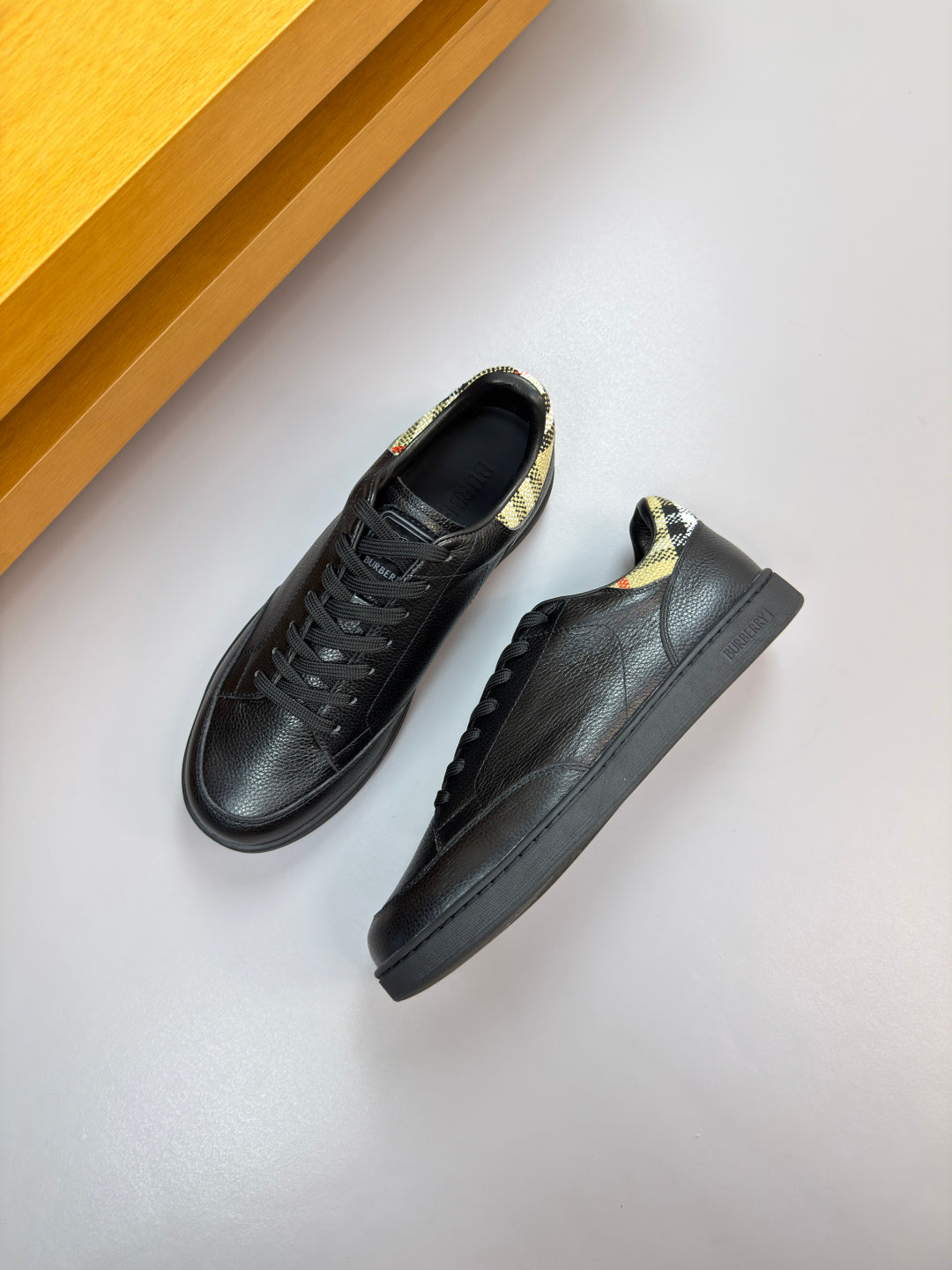 Black leather lace-up sneakers with Burberry check lining at collar and rubber sole.