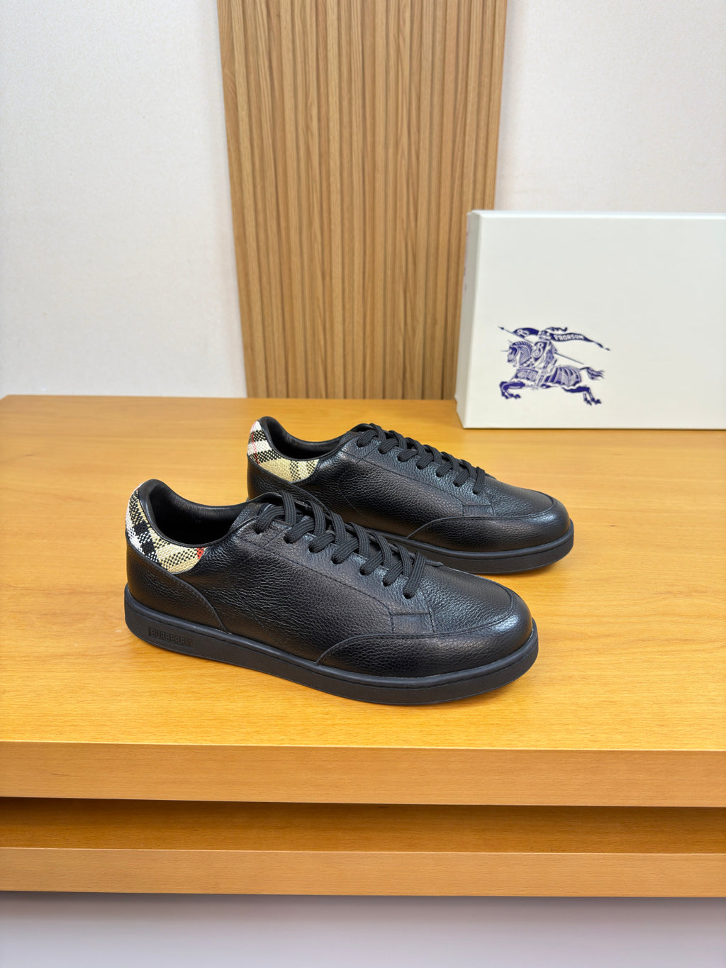 Black leather lace-up sneakers with Burberry check trim at heel and rubber sole.