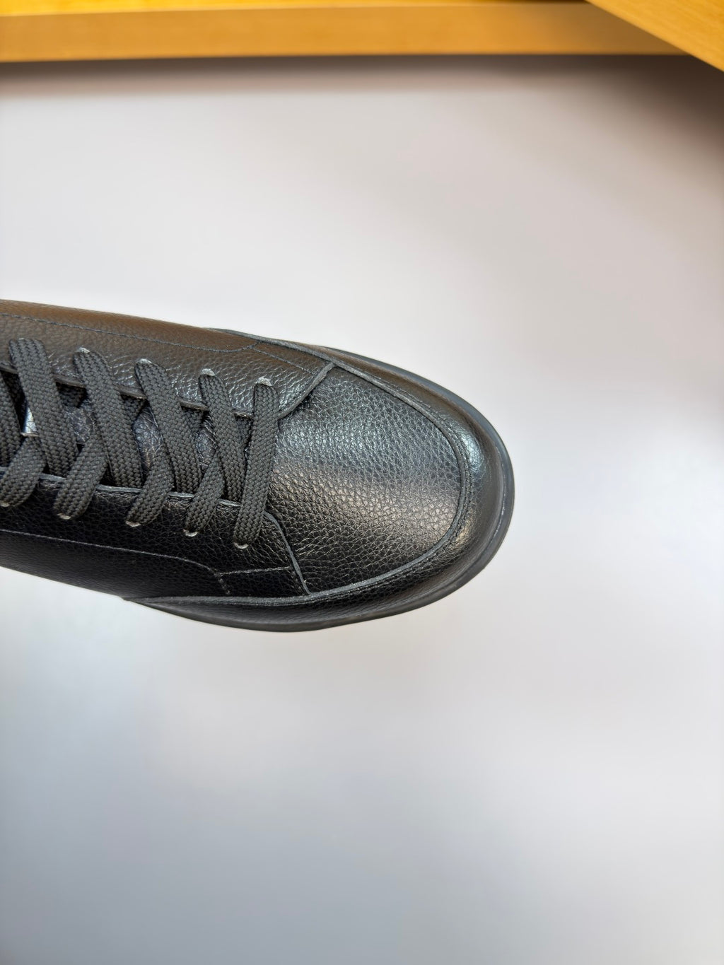Side view of dark leather low-top sneaker with black laces and textured toe panel