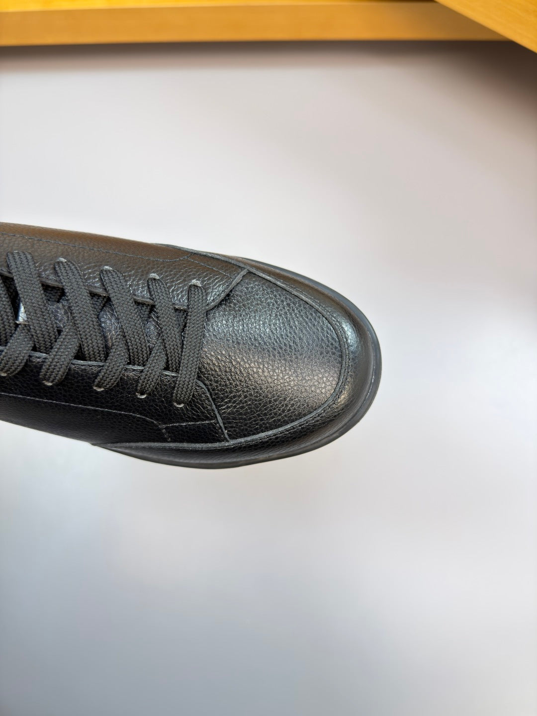 Side view of dark leather low-top sneaker with black laces and textured toe panel