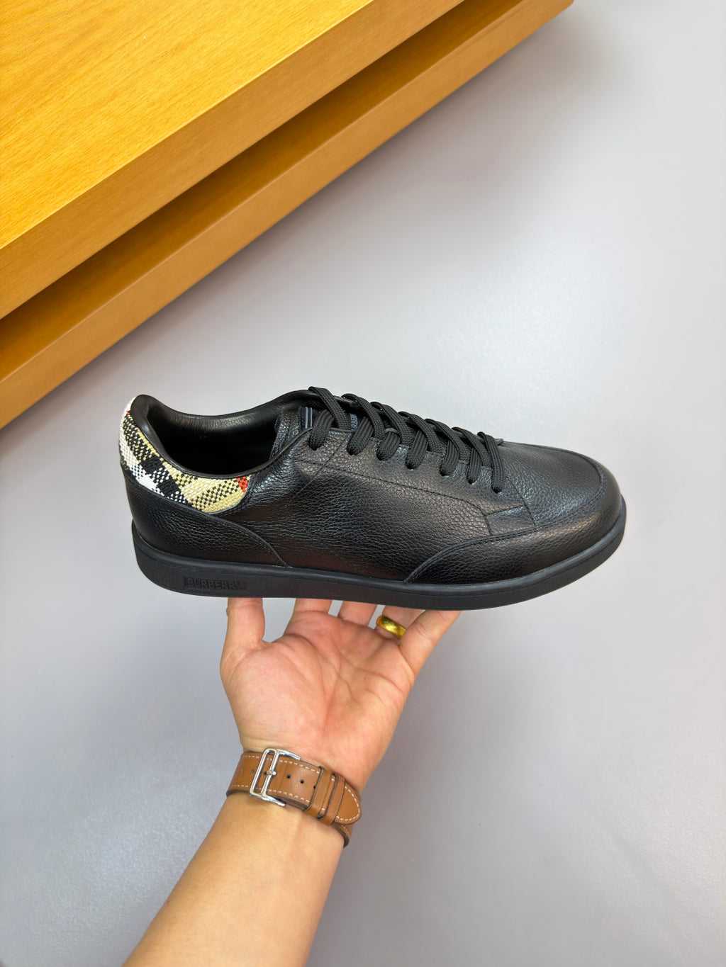 Black leather lace-up sneaker with Burberry check lining at collar, side view.