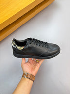 Dark leather low-top sneaker held by hand; black laces with patterned collar trim