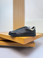 Black leather lace-up sneaker with Burberry check detail at collar, on display stand.