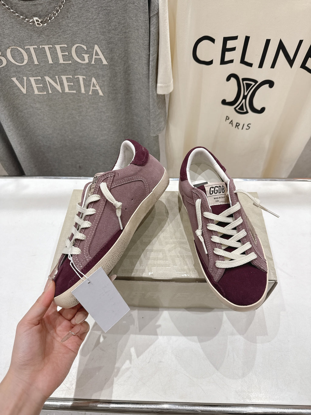 Maroon suede sneakers with white laces, shown in hand, beige sole.
