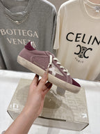 Maroon suede sneaker with white laces, held up, beige rubber sole.
