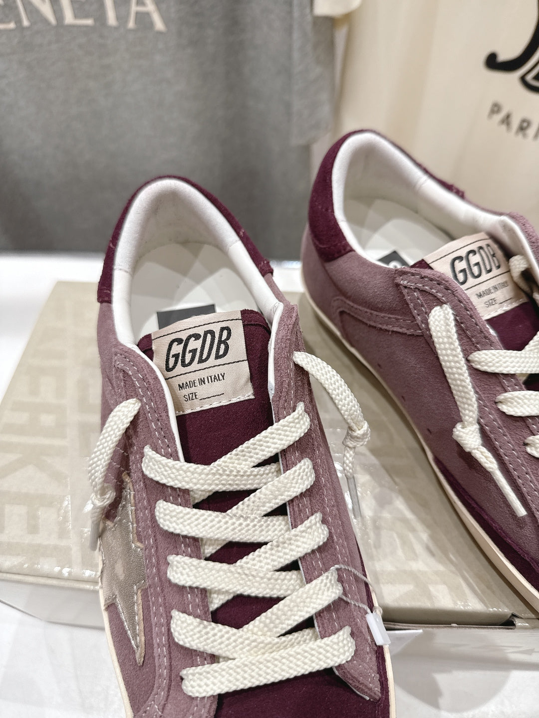 Maroon suede sneaker with white laces and GGDB label on tongue, close-up.