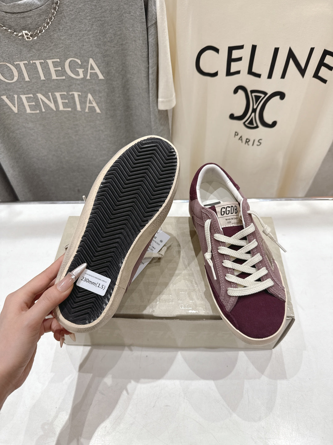 Maroon suede sneakers with textured outsole, one shoe sole shown by hand.
