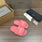 Pink terry slide sandals with logo strap detailing, pair laid flat on the floor.