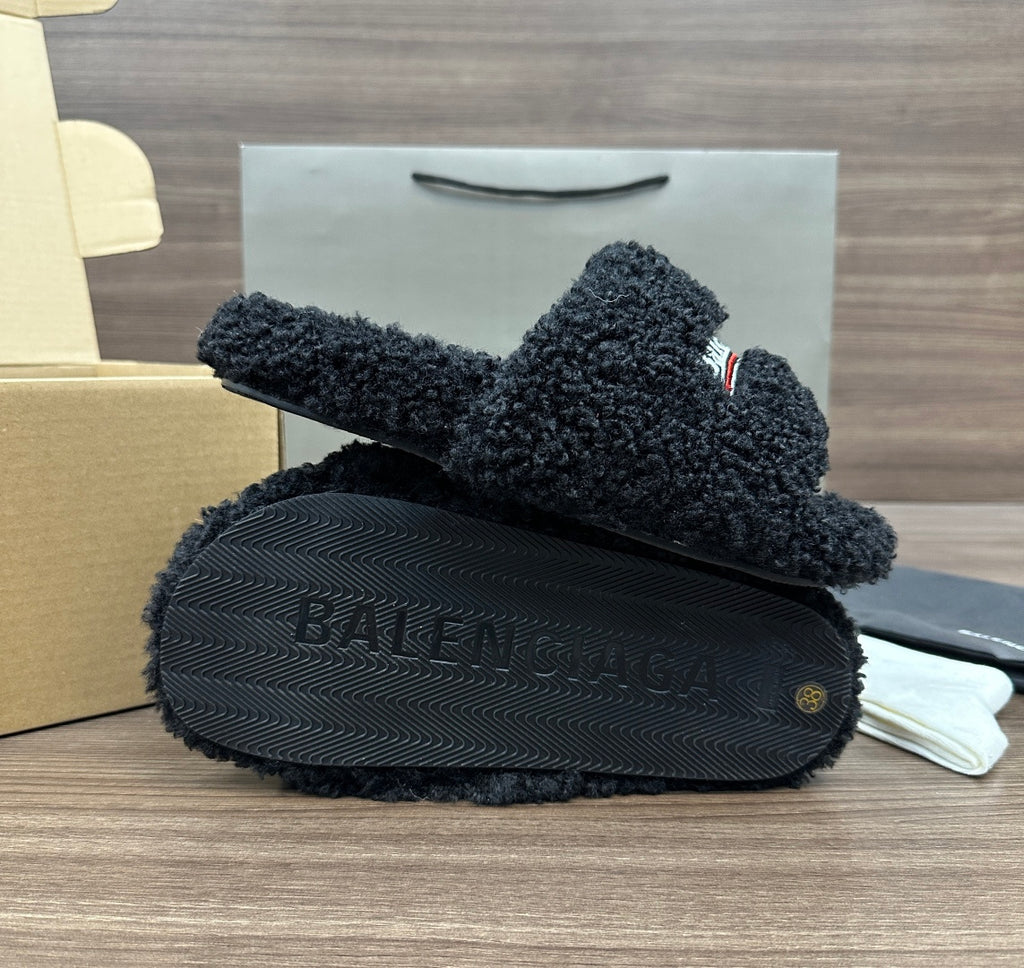 Black plush slide sandals with textured tread sole, logo strap visible