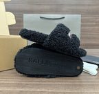 Black plush slide sandals with textured tread sole, logo strap visible
