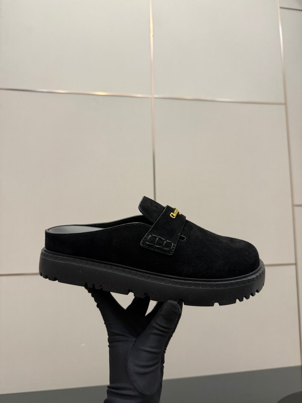 Black suede mule with strap and gold buckle detail, chunky tread sole